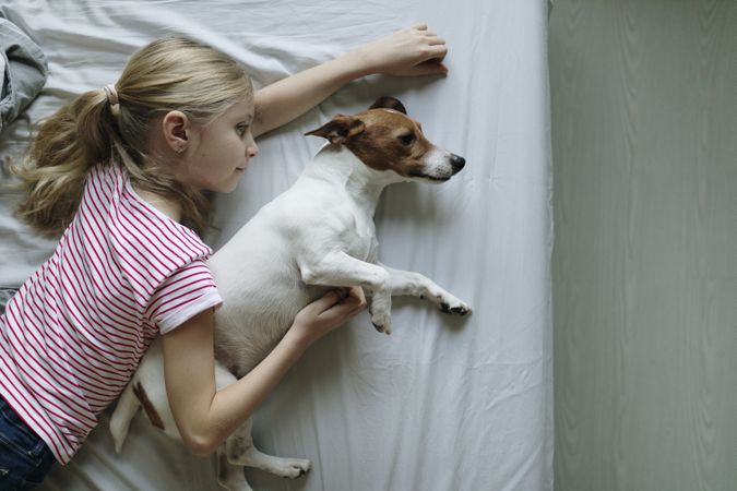 Top view of young blonde girl spooning her dog in the bed