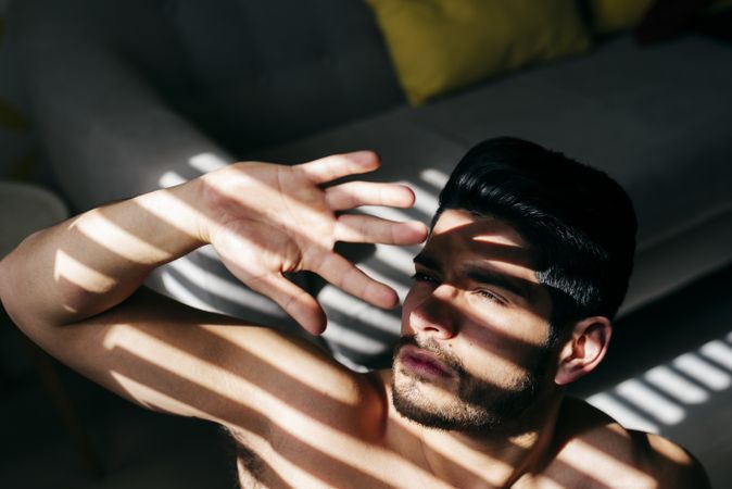 Young naked man covering sunlight with hand