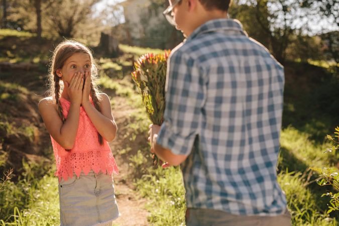 Surprised girl standing with hands on mouth looking at the flowers in the hands of her boyfriend