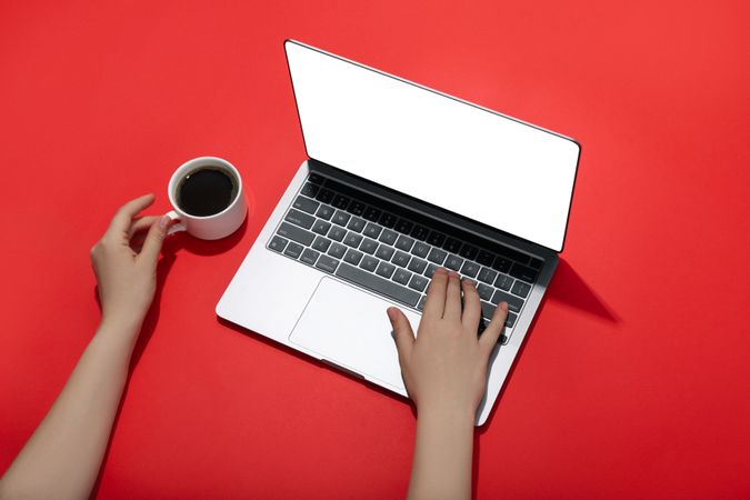 Top view of person typing on laptop keyboard on red table with coffee