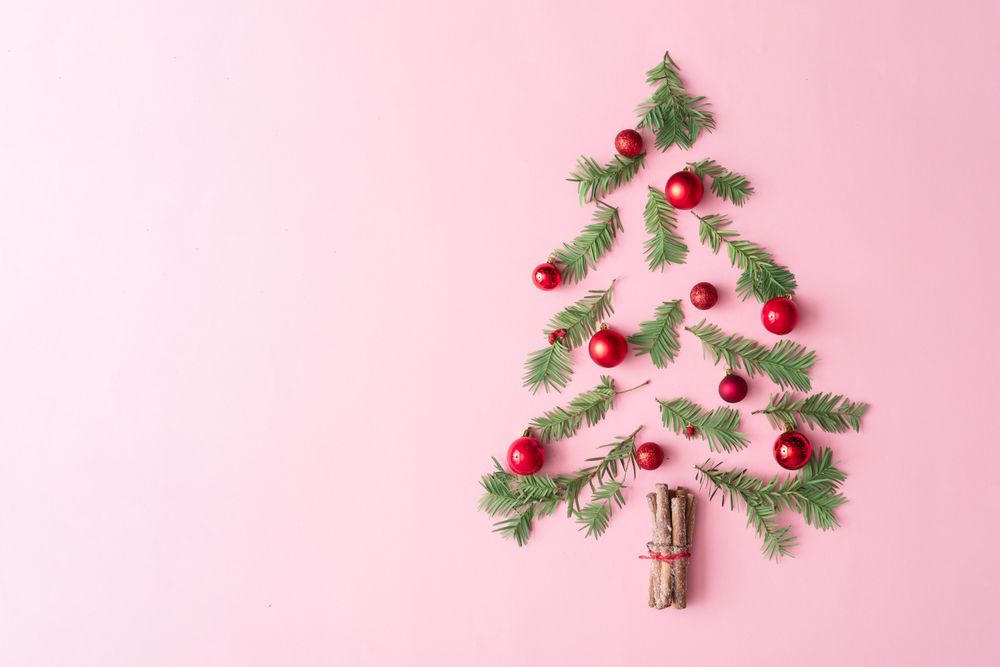 Christmas tree made with evergreen fir, bauble decoration and cinnamon sticks on pink background