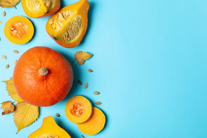 Composition with pumpkin, slices, leaves and seeds on blue background