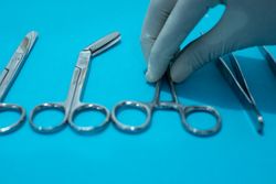 Hand doctor taking scissors or forceps surgical instrument on blue background