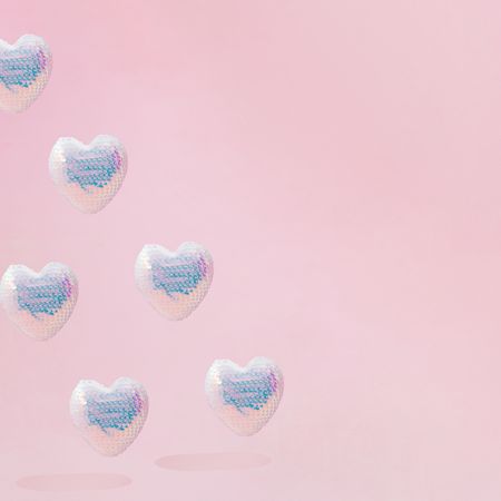 Pattern of iridescent sequins hearts on pink background with copy space
