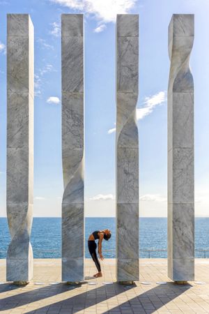 Side view of female doing yoga between sculpture with ocean view