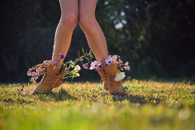 Crop person wearing boots with flowers standing on grassy glade