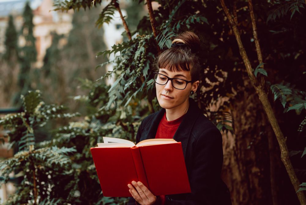 Young woman reading book on bench in park