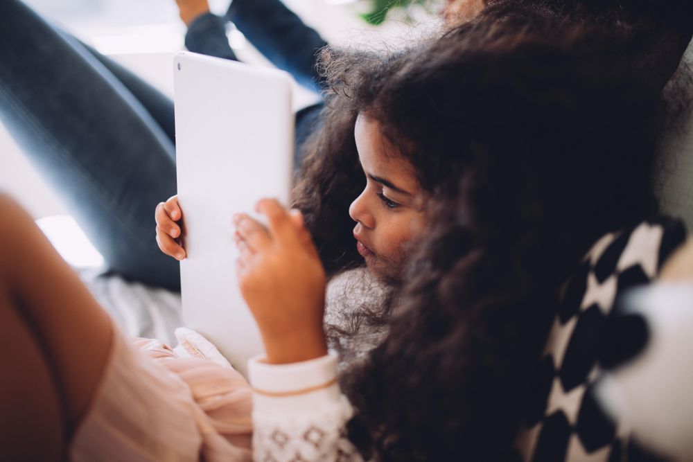 Little girl lying in bed reading a tablet
