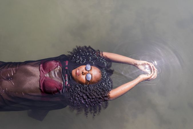 Beautiful young Black woman floating in a pool of water in the sun