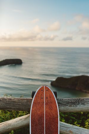 Surf skate leaning on wooden railing against blurred beach