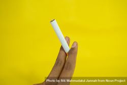 Hand holding cigarette against yellow wall 4d872E
