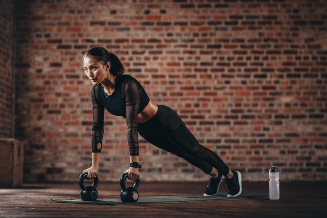Fitness woman doing push-ups with kettlebells at gym