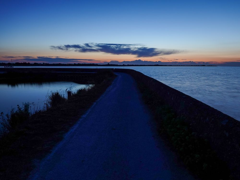 Sunrise illuminating the path of the dike at high tide
