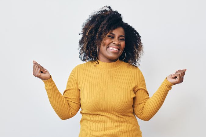 Studio shot of a happy Black woman in yellow shirt with her arms up and eyes closed