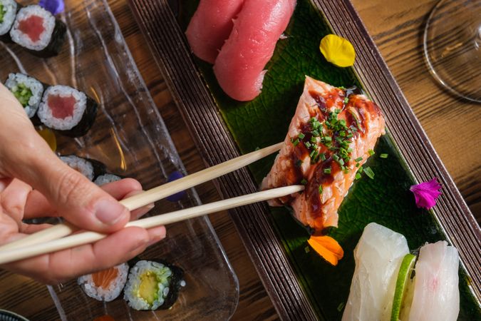 Person with chopsticks eating sushi with soy sauce