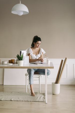 Woman with her hair pulled back wearing a white top and blue jeans writing in a notebook at a table