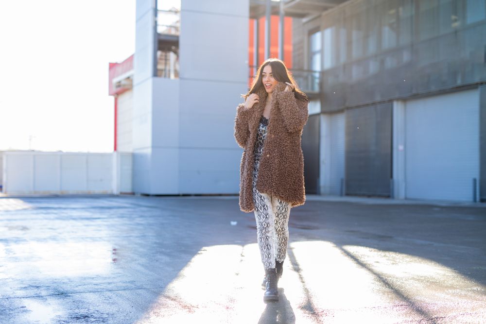 Cheerful woman wrapping in coat on street