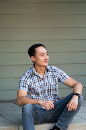 Man in plaid shirt sitting on steps in front of house smiling and looking away
