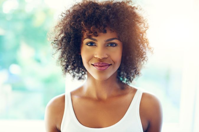 Confident female looking at camera with curly hair on leafy background, copy space