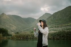 Woman drinking water near lake between mountains