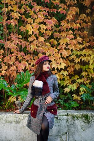 Female standing in front of wall with orange yellow fall leaves, vertical composition