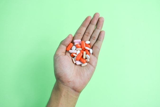 Variety of colorful medication and vitamins in hand above green table