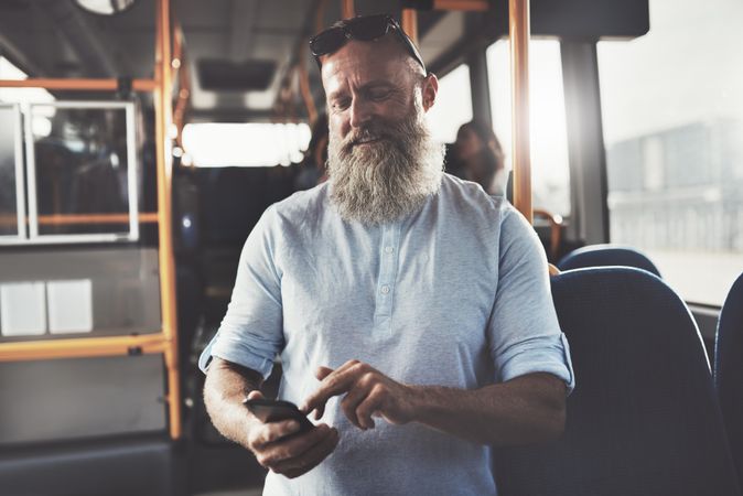 Man with gray beard smiling while texting on public transport