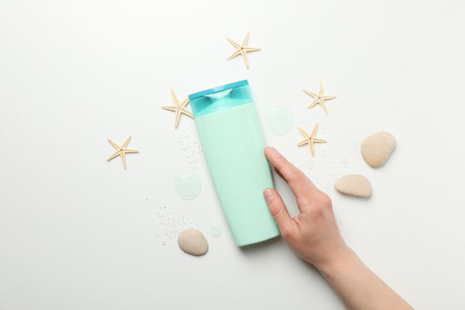 Female hand touches a bottle of shampoo on light background