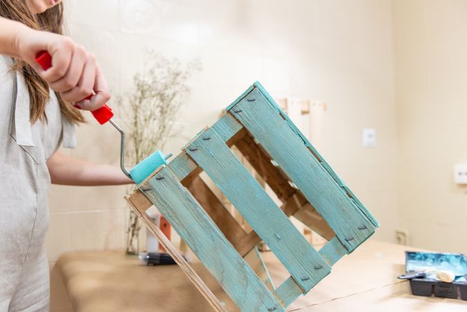 Woman paining wooden box in blue color with roller