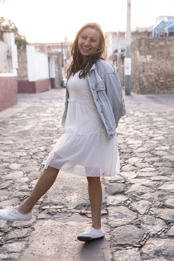 A young Hispanic woman with sunglasses is smiling posing in the street during the sunset