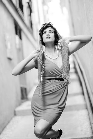 Elegant woman in dress holding onto her lace scarf standing on outdoor stairs