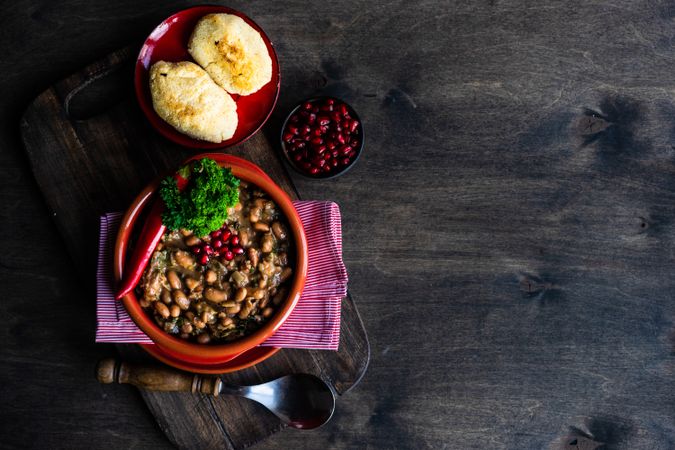 Top view of Georgian bean dish with rolls and pomegranates on wooden table with copy space