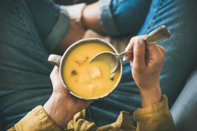 Woman in jeans and yellow shirt holding spoon with cup of squash soup
