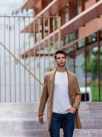 Young man in jeans and autumn coat walking down stairs outside