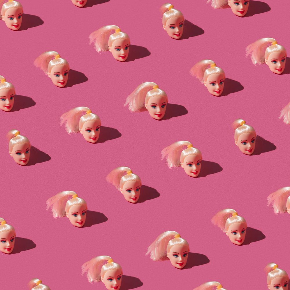 Pattern made of doll heads on pink background