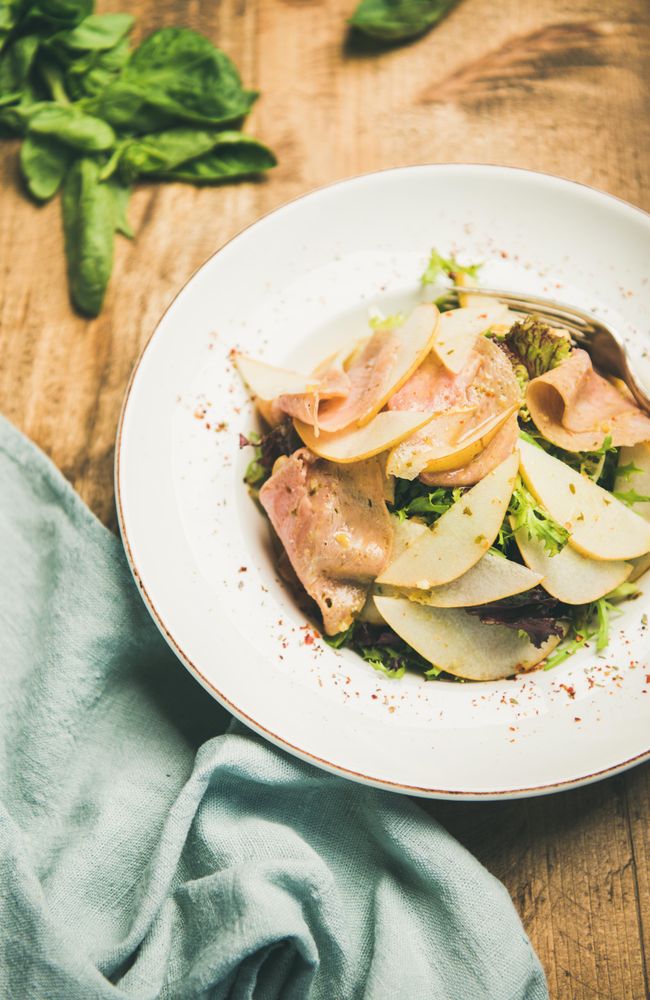 Top view of ham and pear in bowl, on wooden background with linen napkin and spinach