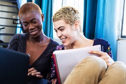 Smiling female friends woman with laptop resting on couch at home