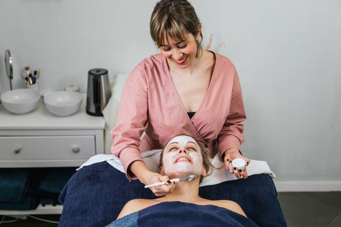Professional beautician applying facial mask on face of client