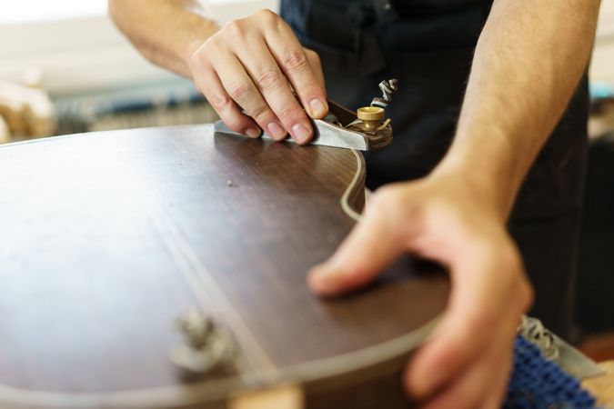 Cropped shot of male hands shaving back of guitar in luthier workshop