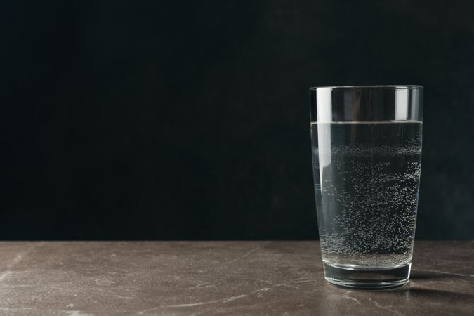Single glass of water in dark room on marble table, copy space