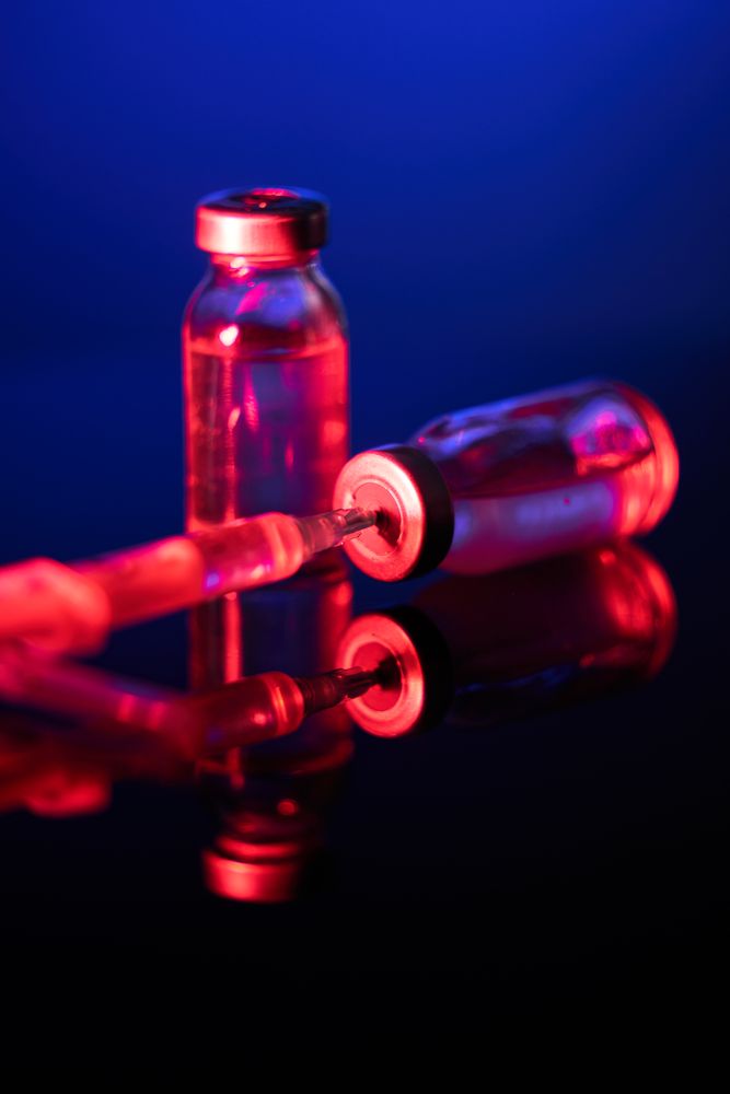 Syringe inserted into vial under neon lighting