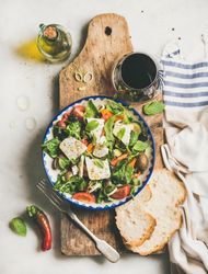 Greek salad with feta, tomatoes, and red wine on wooden board, vertical composition