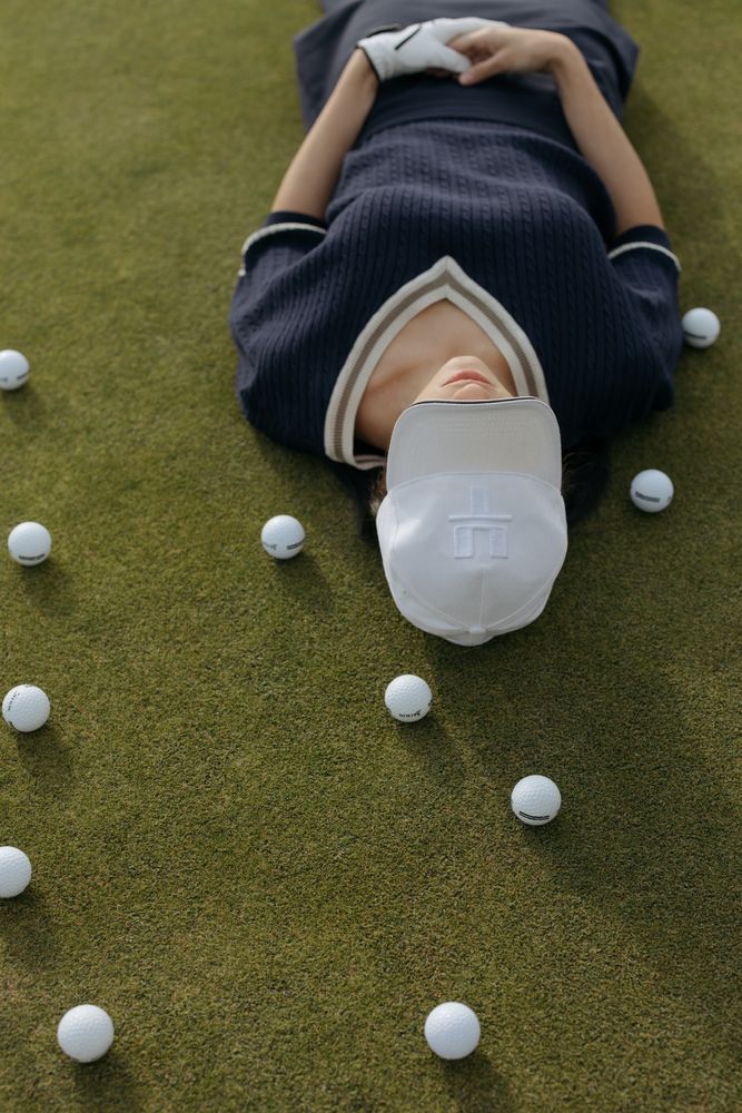 Woman laying on green grass beside golf balls