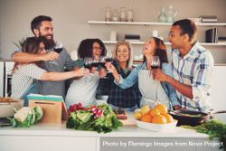 Group of friends toasting with red wine as they cook together at a dinner party 5QOXgb