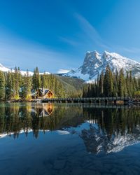 Brown wooden house on lake near snow covered mountain with reflection on water