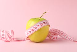 Measuring tape with apple on pink background, weight loss