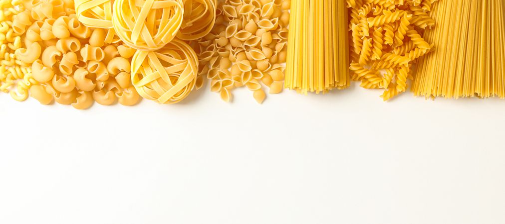 Different pasta on light background, space for text. Dry uncooked whole pasta