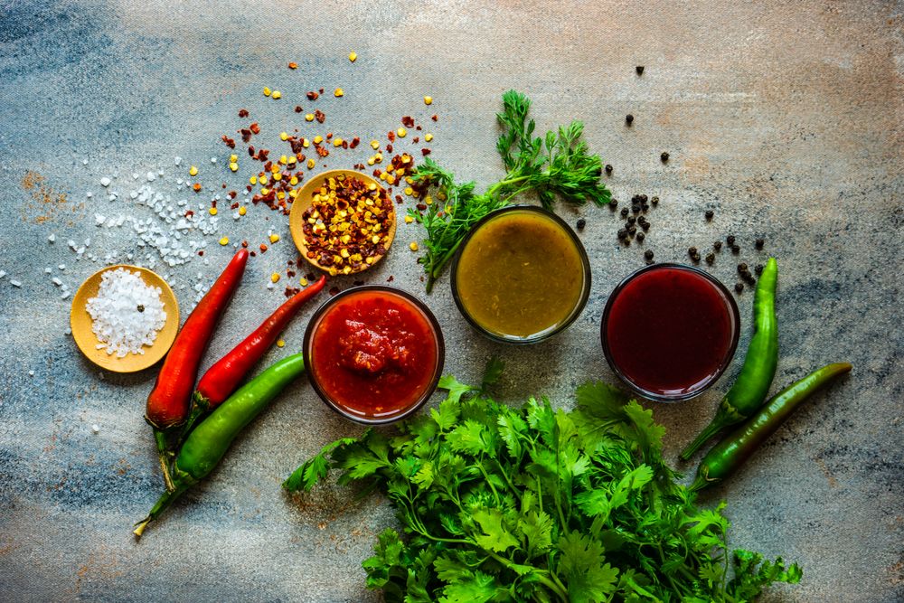 Top view of traditional Georgian sauces tomato satsebeli, yellow and red tkemali with ingredients on grey counter