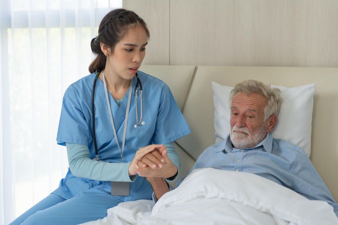 Asian female caregiver holding older man’s hand giving support and empathy
