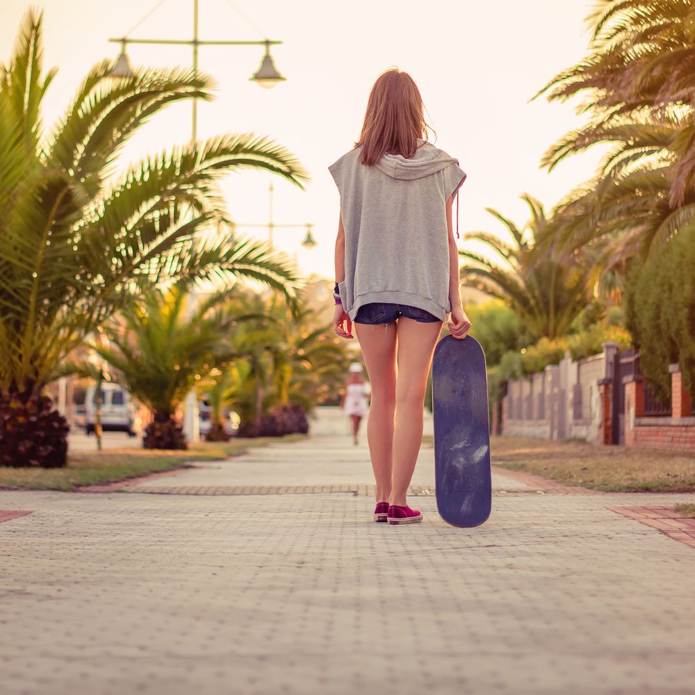 Back view of girl with a skateboard outdoors on summer